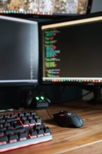 Modern computer monitors with programming code placed on desk with keyboard and mouse